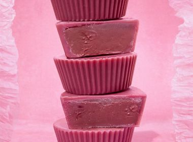 Fünf gestapelte pinke Bio Nut Butter Cups Double Raspberry von KoRo vor einem rosa Hintergrund. Zwei der Cups sind angeschnitten und zeigen die cremige, dunkelrosane Himbeer-Cashew-Füllung.