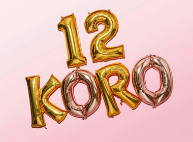 Goldene und rosafarbene Folienballons auf einem rosa Hintergrund, die die Zahl „12“ und den Markennamen „KORO“ bilden.