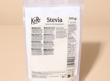 Eine 100-g-Packung KoRo Stevia-Pulver in einem transparenten Standbeutel vor einem schlichten, beigefarbenen Hintergrund.