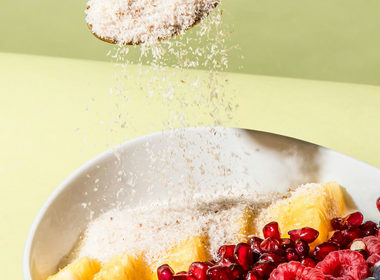 Ein goldener Löffel streut Flohsamenschalen über eine Frühstücksschale mit Ananas, Himbeeren, Heidelbeeren und Granatapfelkernen.