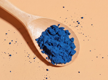 Ein Holzlöffel voller blaues Spirulina-Pulver auf einem hell-orangen Hintergrund. Nahaufnahme von oben.