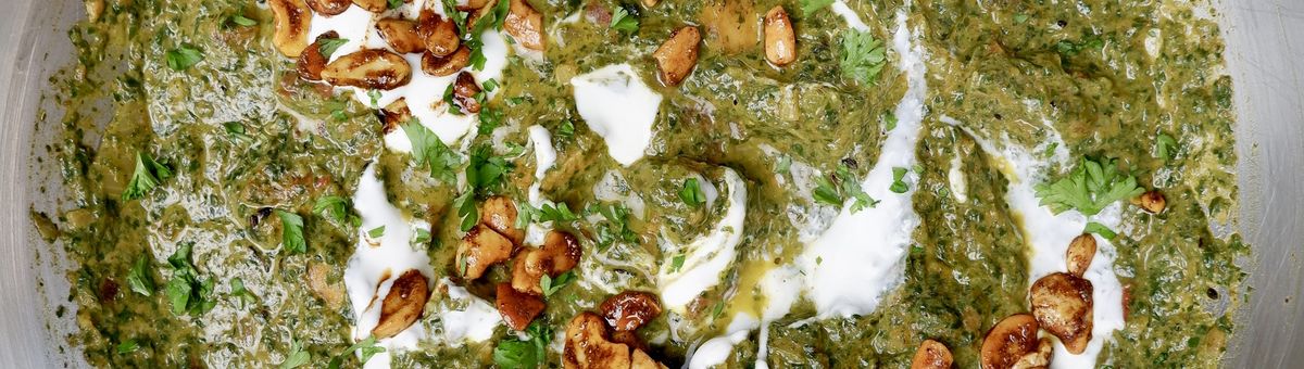 Cremiges veganes Palak Tofu Paneer Curry mit grünem Spinat, goldbraun gebratenem Tofu, gerösteten Cashewkernen, Joghurt und gehackter Petersilie in einer Edelstahlpfanne serviert.