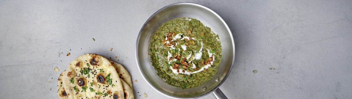 Cremiges veganes Palak Tofu Paneer Curry mit grünem Spinat, goldbraun gebratenem Tofu, gerösteten Cashewkernen, Joghurt und gehackter Petersilie in einer Edelstahlpfanne serviert.