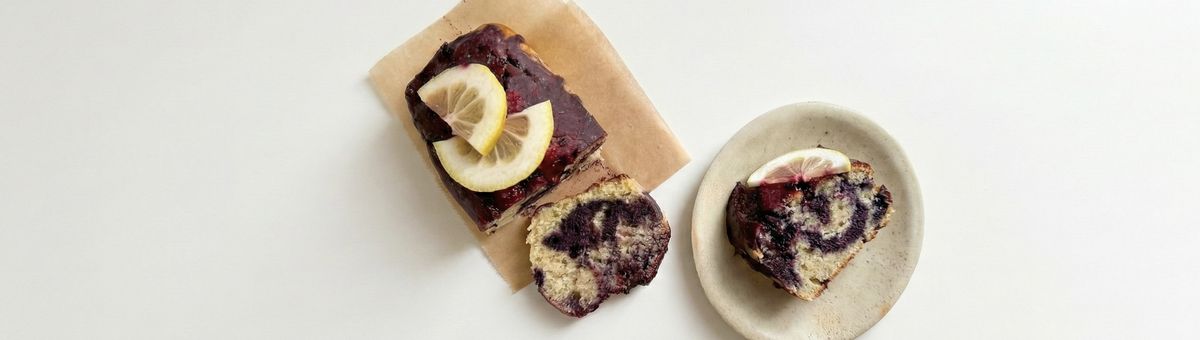 Marmorierter veganer Zitronen-Blaubeer-Kuchen mit Ahorn-Glasur, angeschnitten und auf einem Teller serviert.