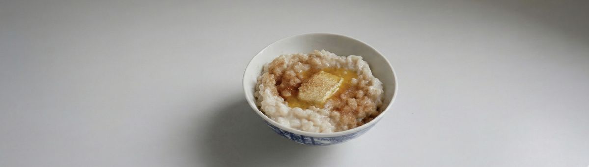 Schüssel cremiger Milchreis mit geschmolzener Butter und Zimt-Zucker auf weißem Hintergrund – klassisches Dessert und süßes Frühstück