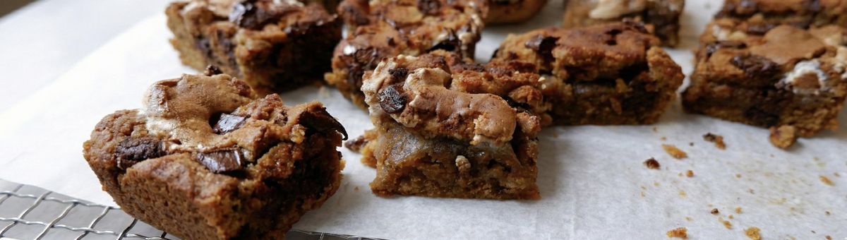 Saftige Kürbis-Blondies mit Schokostückchen und goldbrauner, leicht knuspriger Oberfläche auf Backpapier – herbstliches Gebäck in quadratischen Stücken