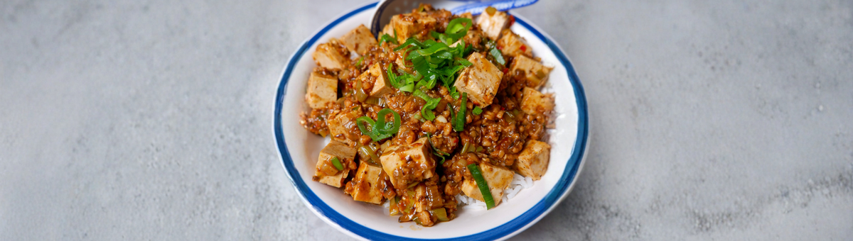 Eine Schüssel serviertes veganes Mapo Tofu: Asiatisches Gericht mit Tofu, Sojagranulat in würziger Sauce und Frühlingszwiebel-Ringen auf einem hellen Hintergrund.