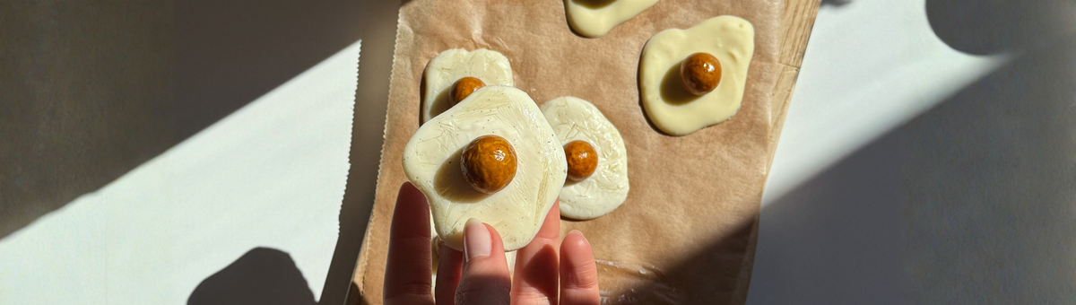 Vegane Spiegeleier aus weißer Schokolade mit gefriergetrockneten Physalis als „Eigelb“ auf Backpapier – kreative Oster-Snack-Idee, handgemacht und dekorativ angerichtet.