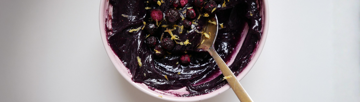 Cremiges Heidelbeer-Zitronen-Mandelmus in einer rosa Schale, garniert mit getrockneten Blaubeeren und Zitronenabrieb.