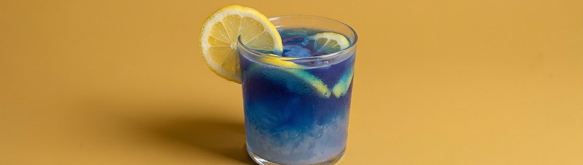 Erfrischende blaue Spirulina-Limonade in einem Glas mit Zitronenscheiben auf gelbem Hintergrund – vegan und glutenfrei.