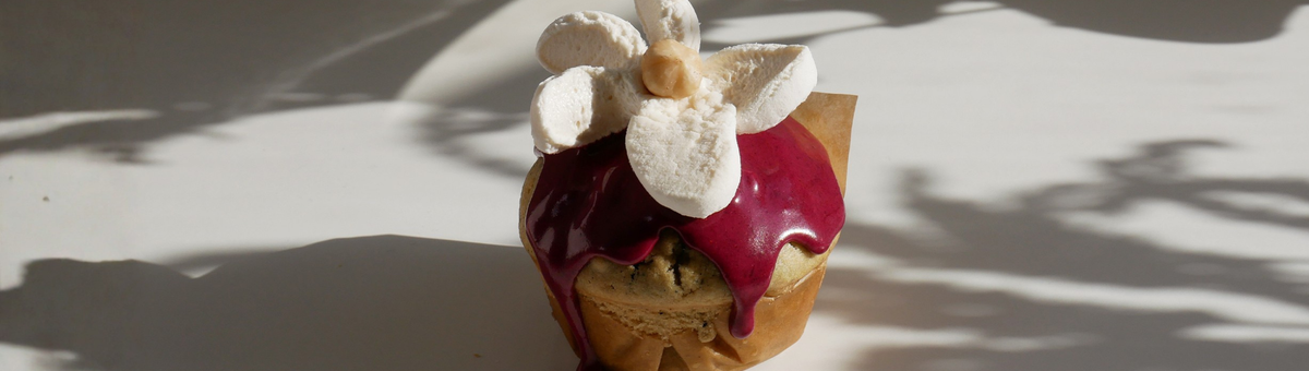 Dekorierter Zitronen-Blaubeer-Muffin mit violettem Heidelbeer-Frosting und weißer Marshmallow-Blüte in Nahaufnahme.