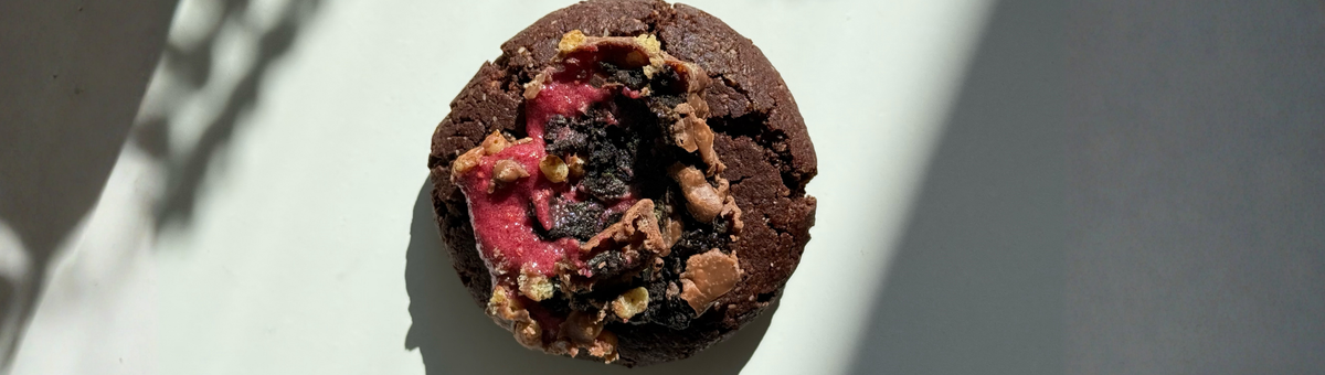 Ein saftiger veganer Schokoladen-Cookie auf hellem Untergrund, großzügig getoppt mit Stücken eines Raspberry Brownie Proteinriegels.