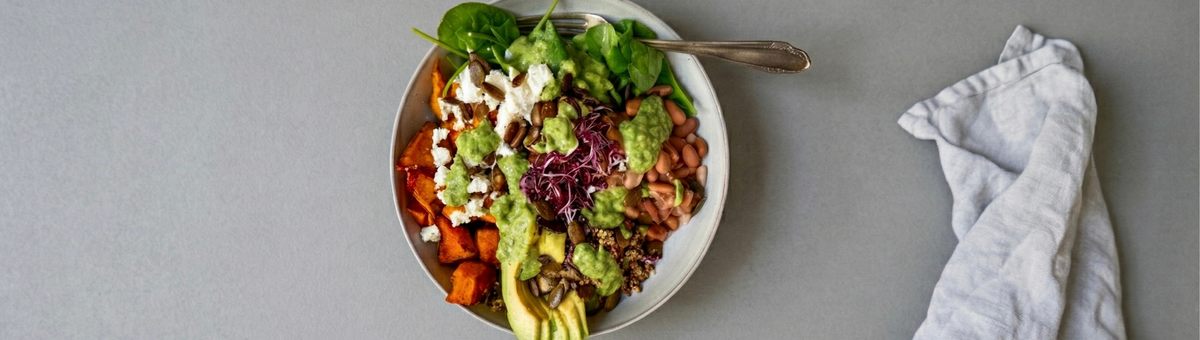 Kürbis-Bowl mit Pinto Bohnen, Hokkaido-Kürbis, Quinoa und Babyspinat auf grauem Hintergrund. Garniert mit Feta, Avocado, Sprossen und gerösteten Kürbiskernen.