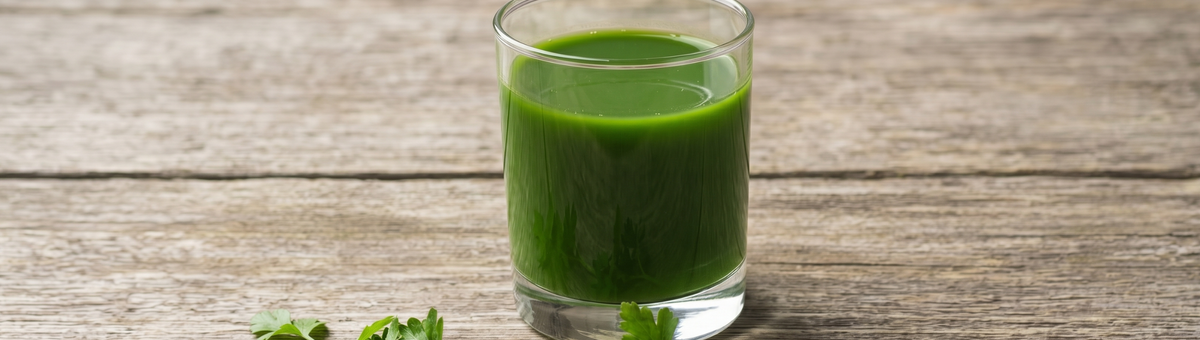 Grüner Smoothie aus Sellerie und Weizengras in einem Glas auf rustikalem Holztisch, Seitenansicht im Panoramaformat.