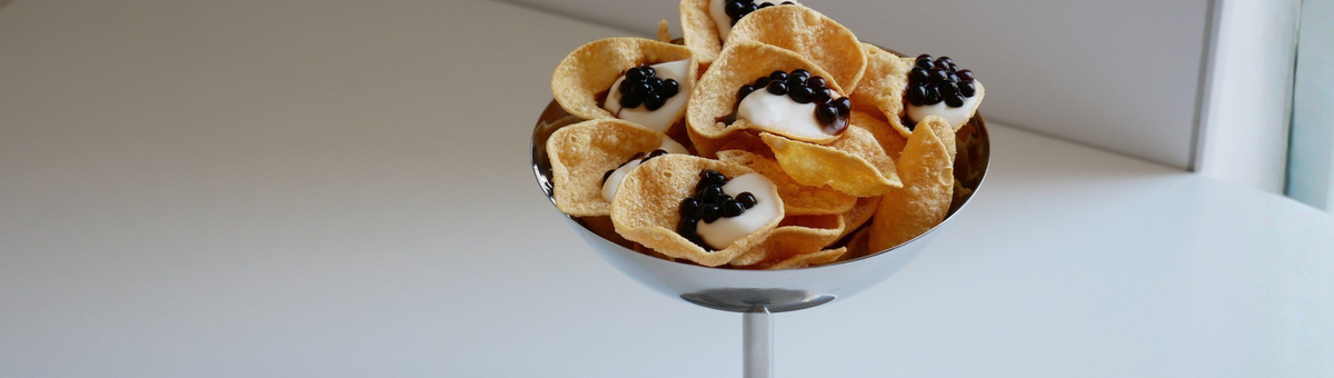 Veganer Vorspeisen-Snack: Knusprige Linsenchips angerichtet mit cremiger Yuzu-Mayonnaise und dunklen Essigperlen in einer edlen Metallschale.