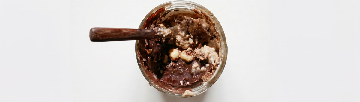 Cremige Schoko-Haselnuss-Overnight-Dinkelflocken im Glas mit ganzen Nüssen und einem Löffel serviert.