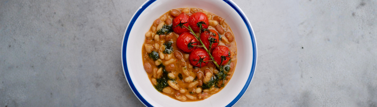 Veganer One-Pot-Bohneneintopf aus weißen und braunen Bohnen, zubereitet mit Olivenöl, Knoblauch und Gewürzen, serviert mit geschmorten Cherrytomaten.