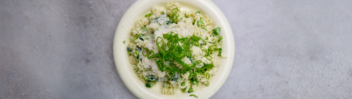 Cremige Pasta al Limone mit Erbsen, geriebenem Parmesan und Frühlingszwiebeln auf einem hellen Teller.