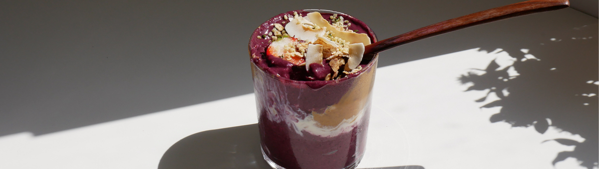 Vegane Acai Bowl im Glas mit Kokosraspeln, Erdbeeren, Hanfsamen und Erdnussbutter im hellen Sonnenlicht.