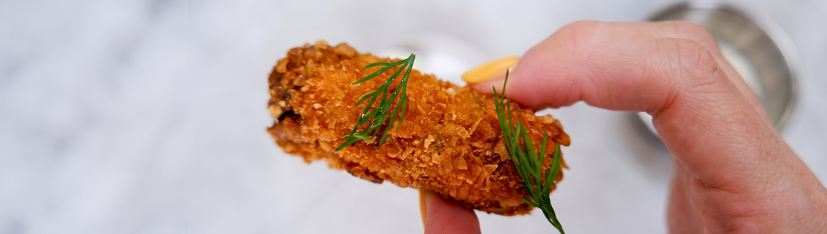 Knusprig frittierte Gewürzgurke (Deep Fried Pickle) mit frischem Dill garniert, serviert als Fingerfood-Snack vor hellem Hintergrund.