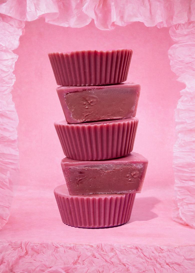 Fünf gestapelte pinke Bio Nut Butter Cups Double Raspberry von KoRo vor einem rosa Hintergrund. Zwei der Cups sind angeschnitten und zeigen die cremige, dunkelrosane Himbeer-Cashew-Füllung.