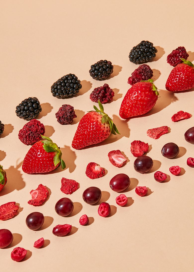 Gefriergetrocknete und frische Beeren wie Erdbeeren, Brombeeren und Cranberries auf hellem Untergrund