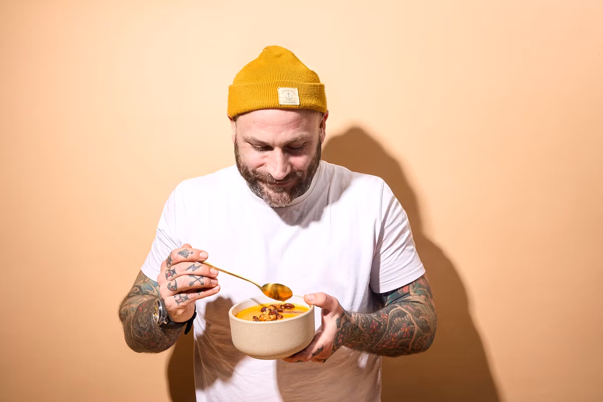 Person hält eine Schale mit cremiger Kürbissuppe, garniert mit crunchy Proteinmix