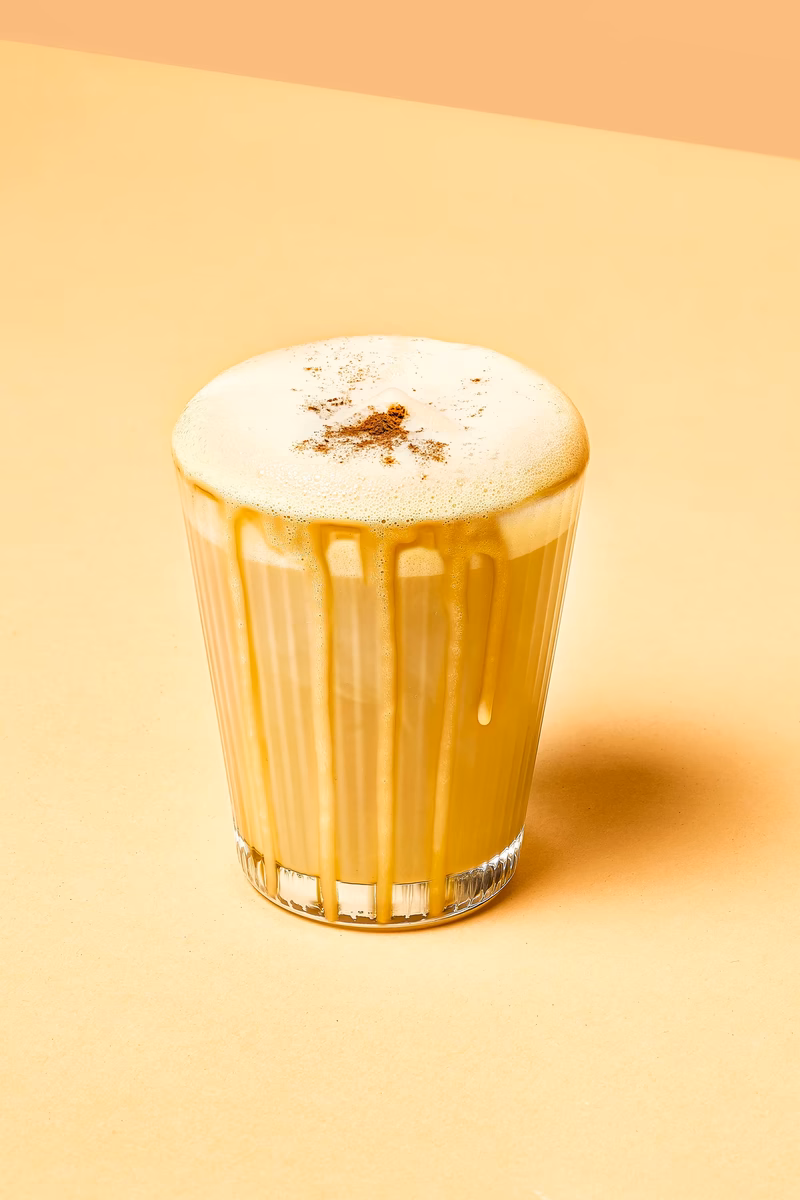 Kurkuma Latte mit Zimt in einem Glas auf hellem Untergrund