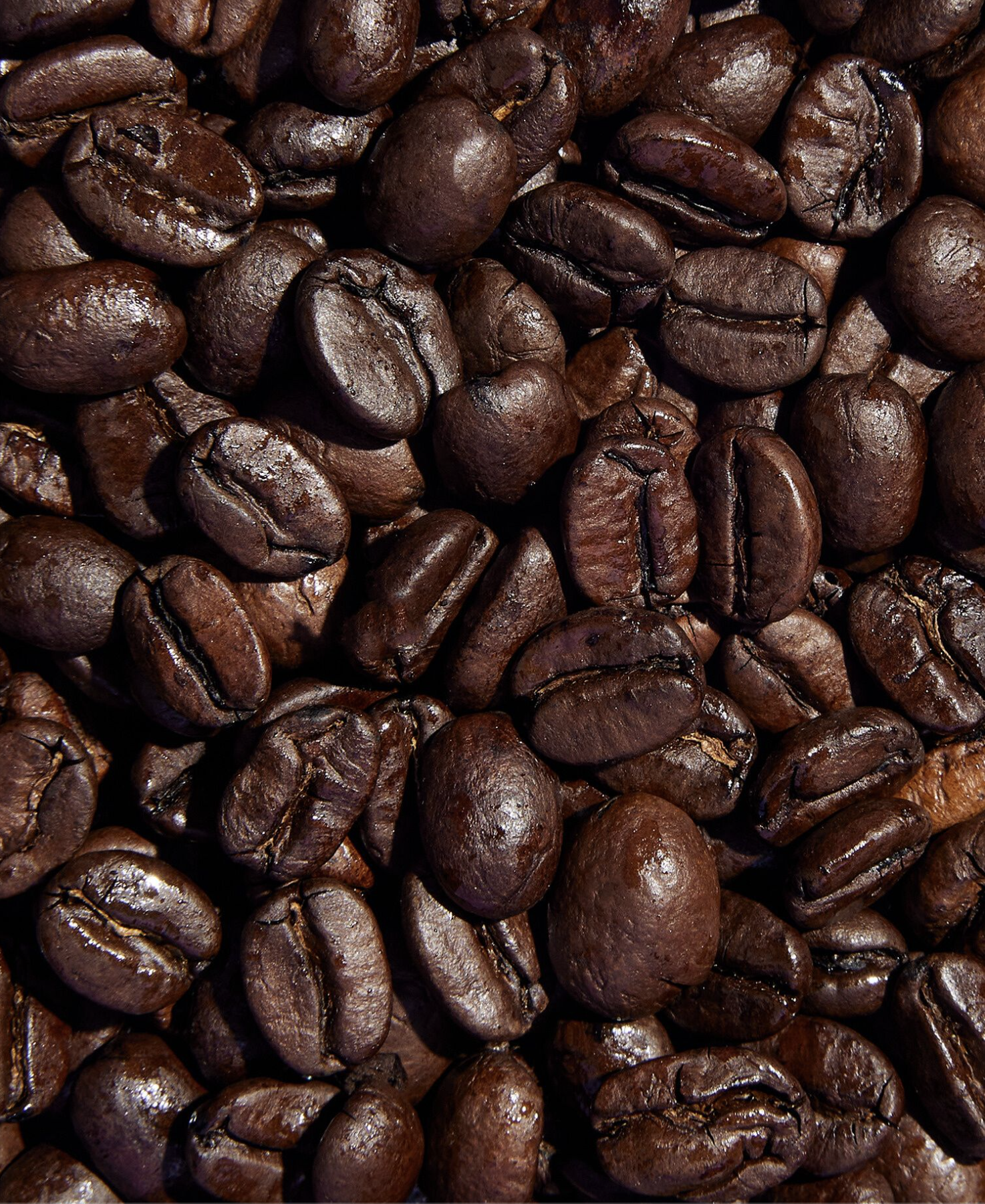 Gros plan de grains de café torréfiés foncés empilés les uns sur les autres.