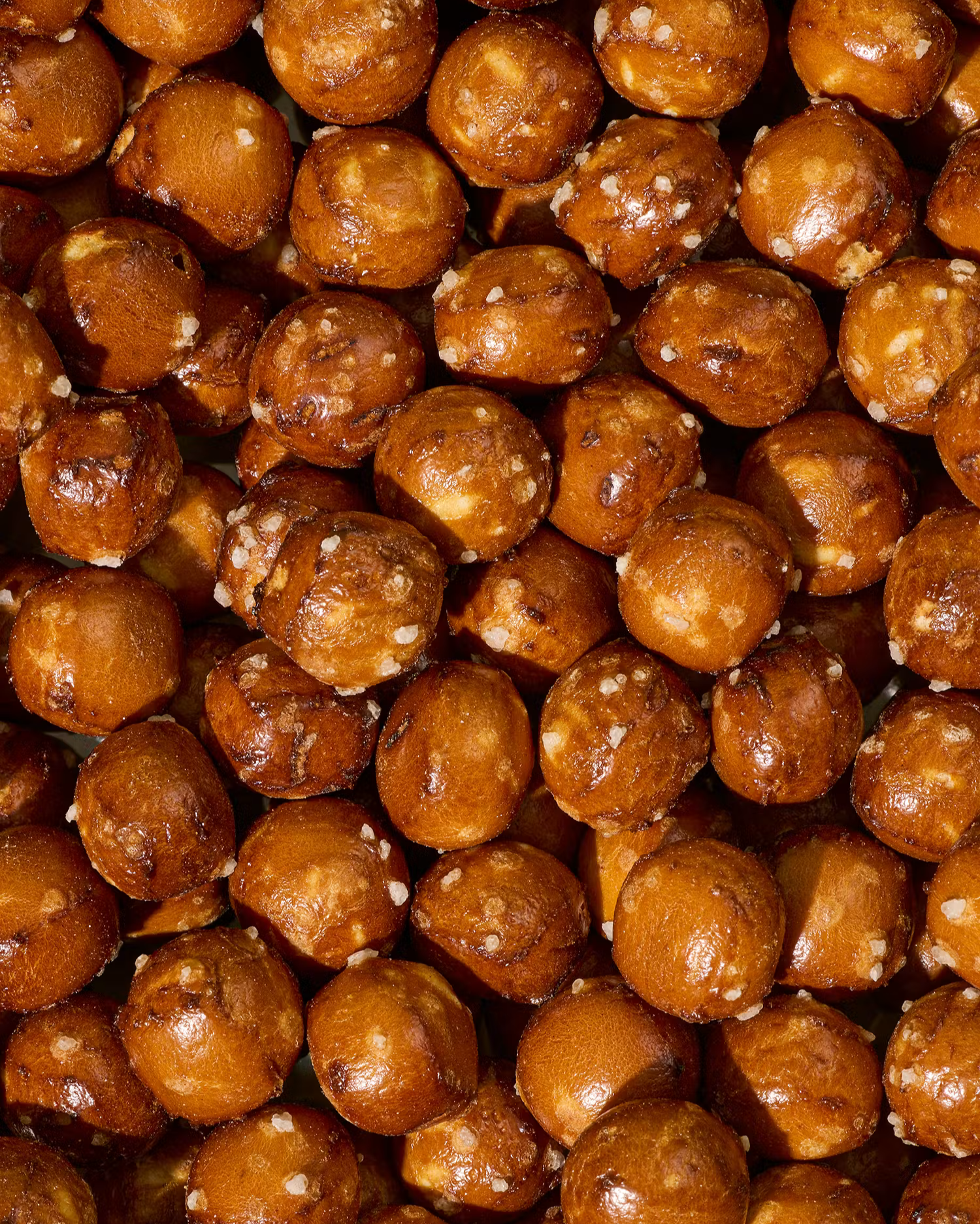Eine Nahaufnahme von vielen runden, goldbraun gebackenen Laugenperlen (Pretzel Balls), die mit groben Salzgitterkristallen bestreut sind.