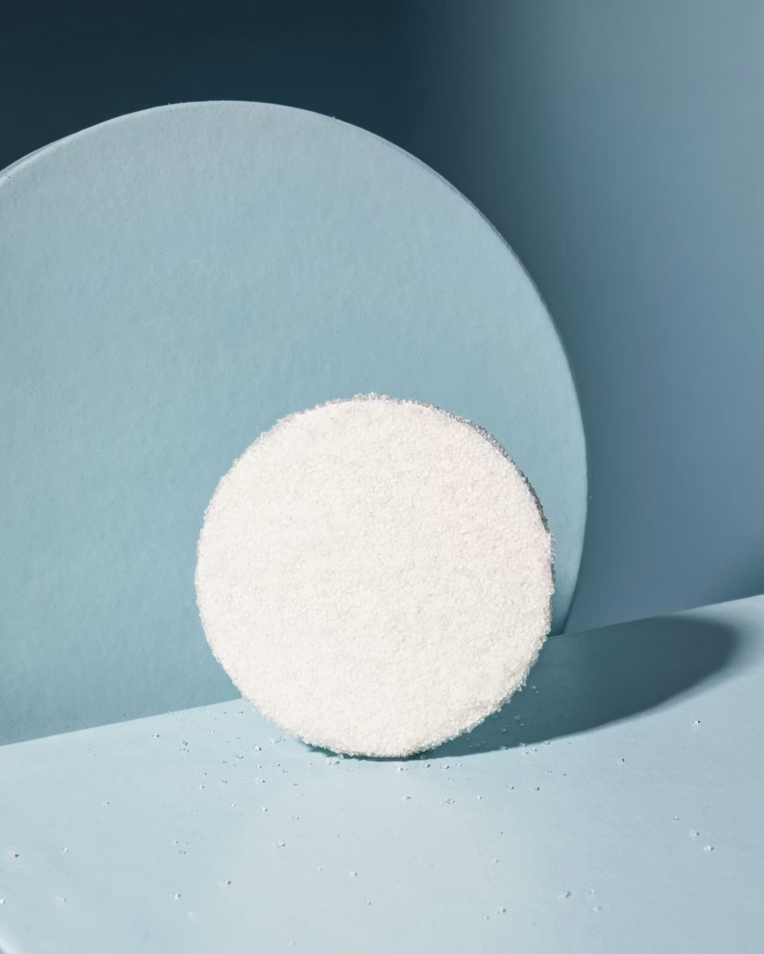 Ein kreisrundes Erythrit-Stück auf einem hellblauen Hintergrund mit geometrischen Formen.