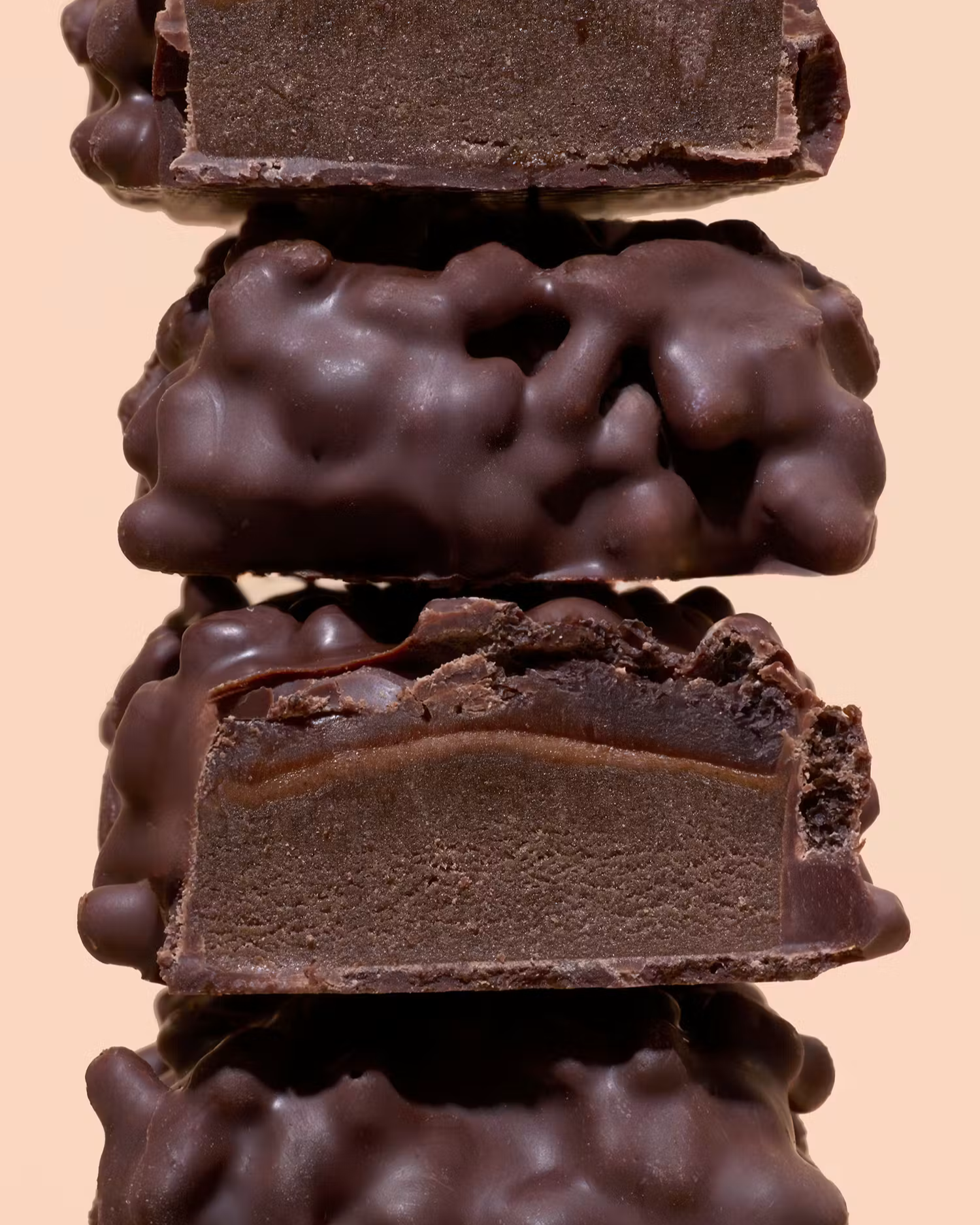 Stapel aus angeschnittenen Schokoladen-Proteinriegeln mit cremiger Füllung und knusperiger Schokoglasur vor hellem Hintergrund.