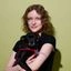 Lisa steht lächelnd vor der Kamera und hat einen schwarzen Hund auf dem Arm, der ebenfalls in die Kamera schaut