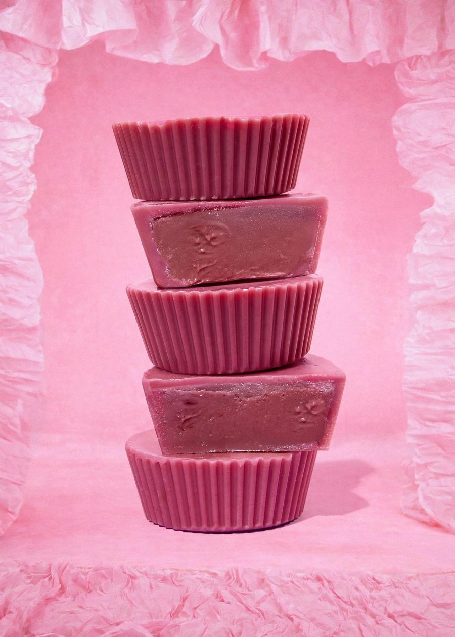 Fünf gestapelte pinke Bio Nut Butter Cups Double Raspberry von KoRo vor einem rosa Hintergrund. Zwei der Cups sind angeschnitten und zeigen die cremige, dunkelrosane Himbeer-Cashew-Füllung.