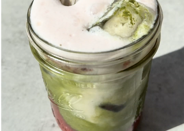 Strawberry Matcha Latte im Glas mit Erdbeerschicht unten, grünem Matcha und Eiswürfeln in der Mitte und rosa Milchschaum oben, mit Glasstrohhalm.