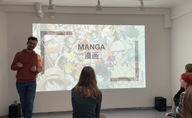 Foredragsholder for mangakurs snakker til deltakere foran lysbildepresentasjon