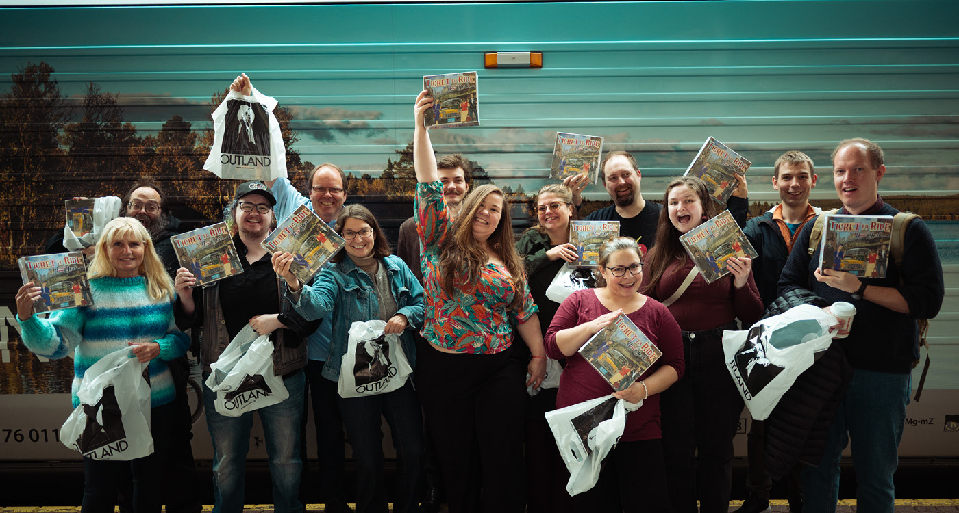 Finalistene fra NM i Ticket to Ride 2025 poserer med Outland-poser foran VY togvogn