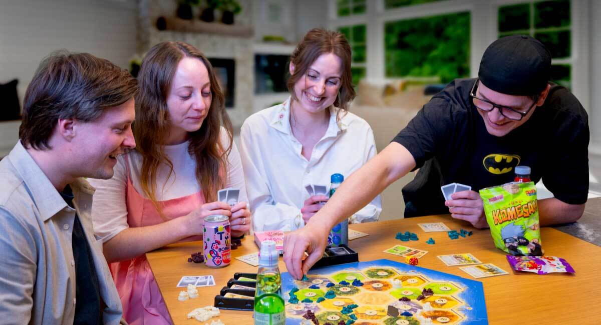 Smilende kolleger spiller brettspill med godteri og brus