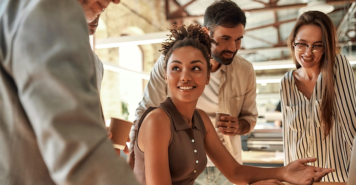 A group of four people having a friendly conversation in a bright office space, one woman smiling. 