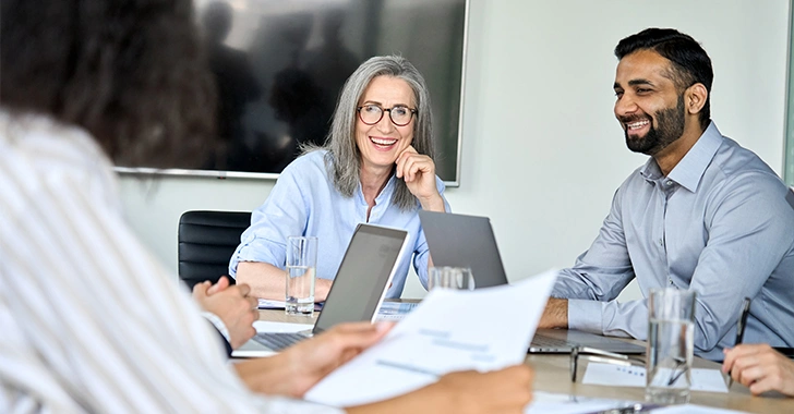 A group meeting with four people at a table. Two are smiling, discussing documents.