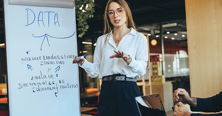 A professional setting featuring a person in a white shirt and glasses presenting data on a whiteboard, with 'DATA' written prominently at the top. 