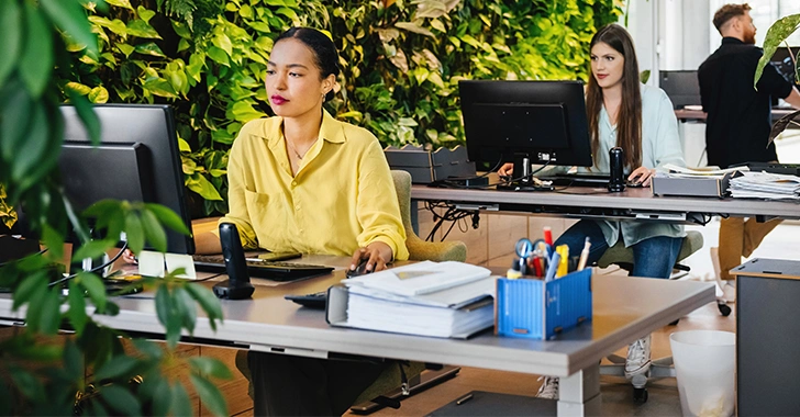An open office space with several people working at desks equipped with computers, documents, and office supplies. 