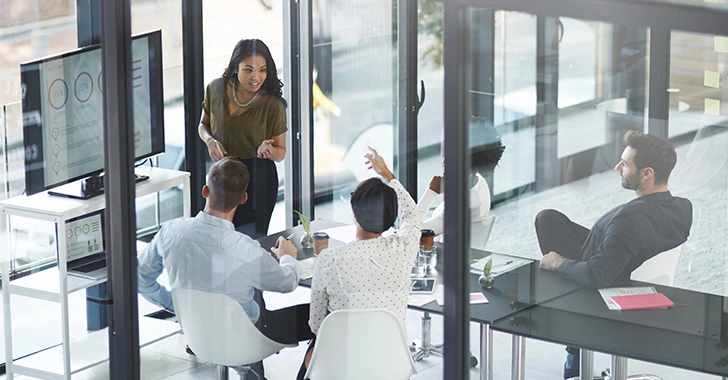 Een groep professionals in een glazen vergaderruimte bespreekt gegevens op een presentatiescherm, terwijl één persoon het gesprek leidt en anderen aan tafel zitten en deelnemen aan de discussie.