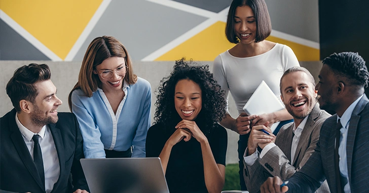 Six diverse professionals collaborate around a laptop in a modern office. 