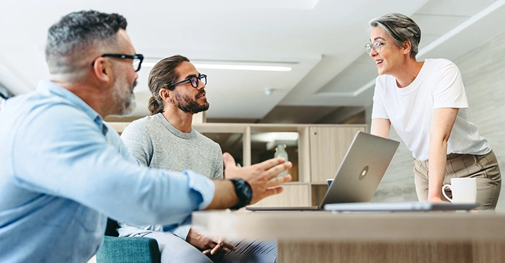 Three colleagues collaborate around a light-colored table in a modern office.