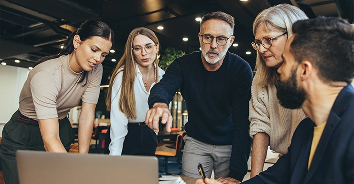 Five professionals collaborate around a table in a modern office.