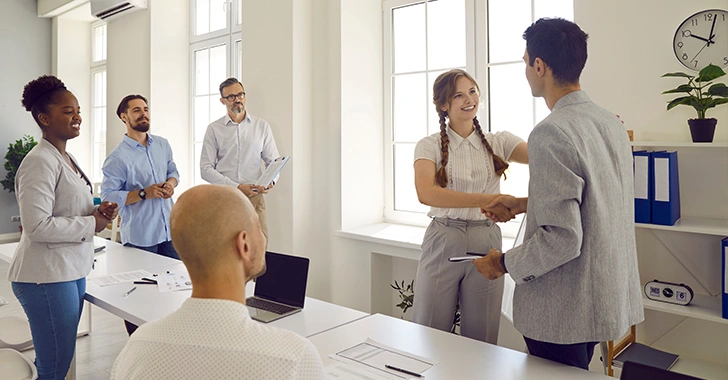 Three professionals collaborate around a light-colored desk in a modern office. 
