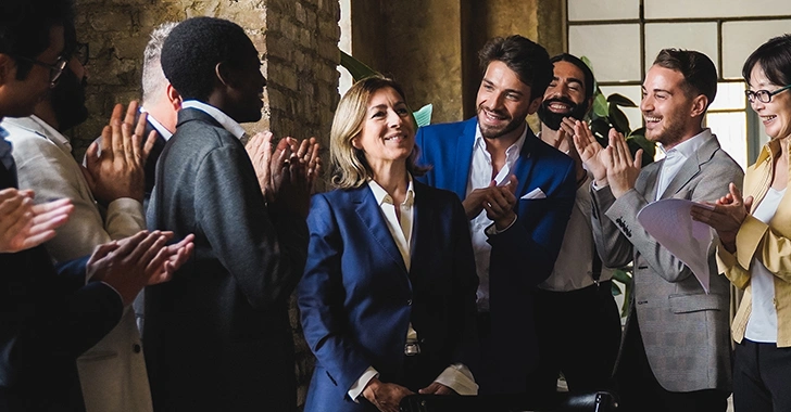 A group of people applauding a woman in a suit, celebrating a success in a bright room. 