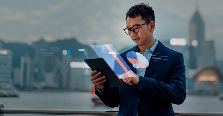 An Asian man in a dark blue suit interacts with a holographic display projected from a tablet.