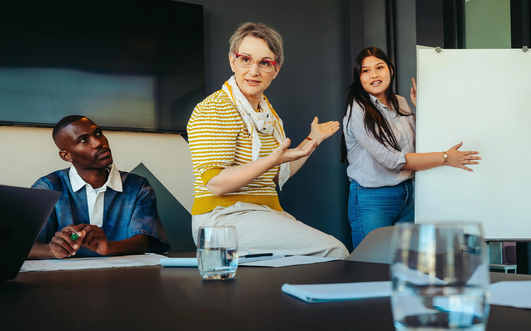 A group of people in a meeting room reviewing information on a whiteboard and documents during a collaborative procurement or contract management workshop.